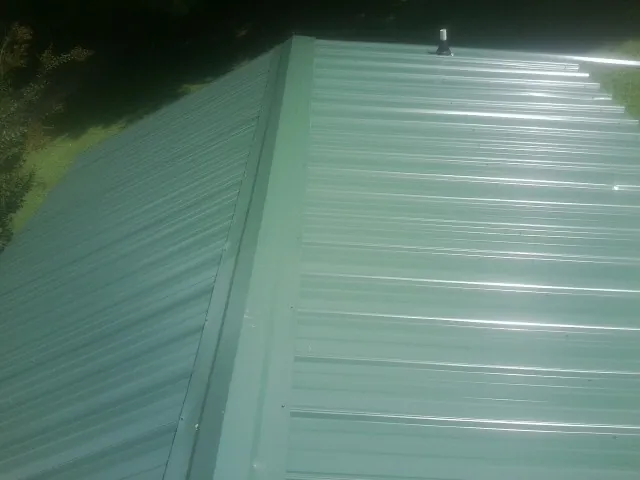 New green metal panels meeting at the ridge of a roof — Flat Roof Repair work by our crew in Jamaica